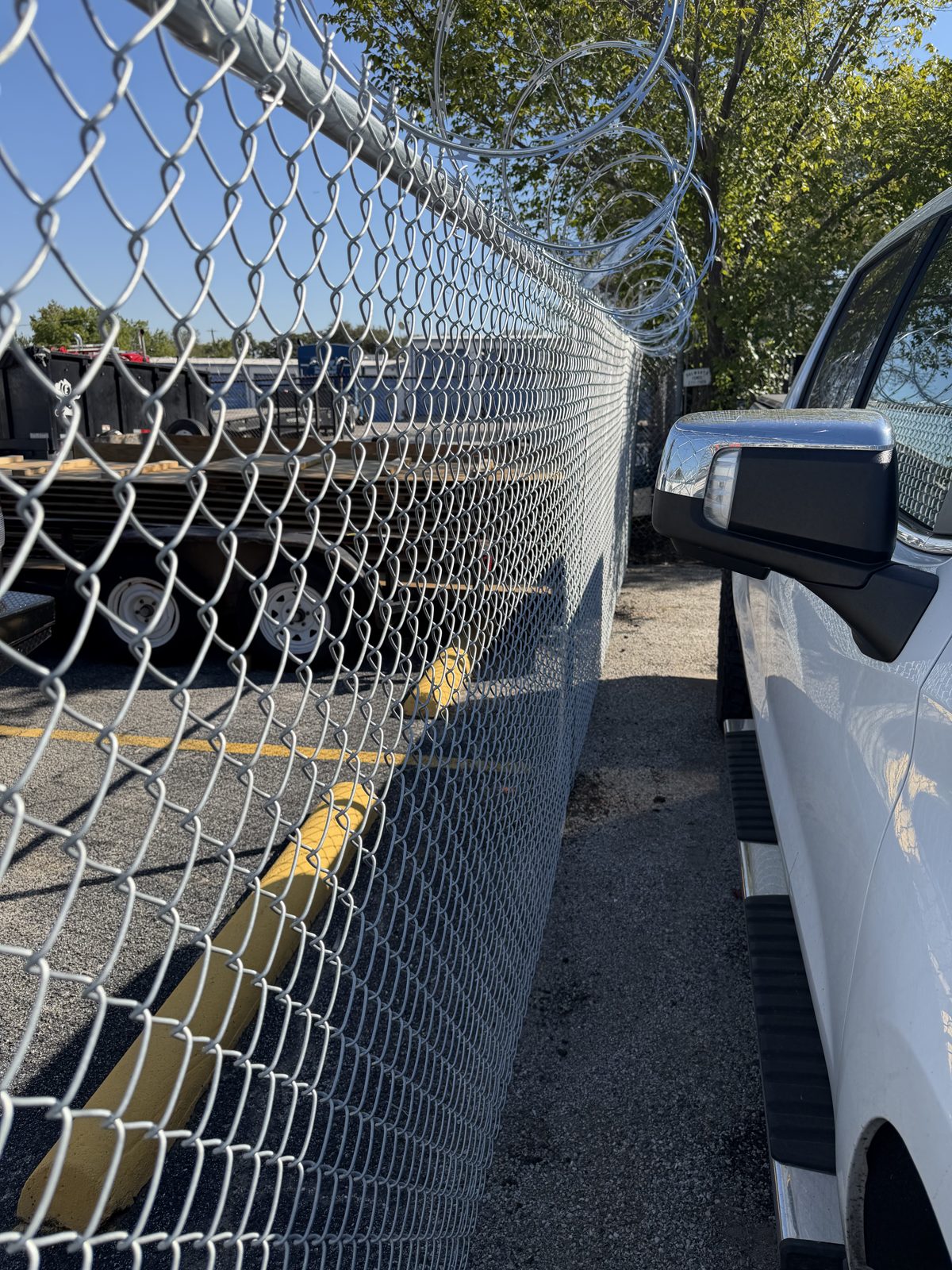 Long chain link fence line topped with razor wire beside a parking area